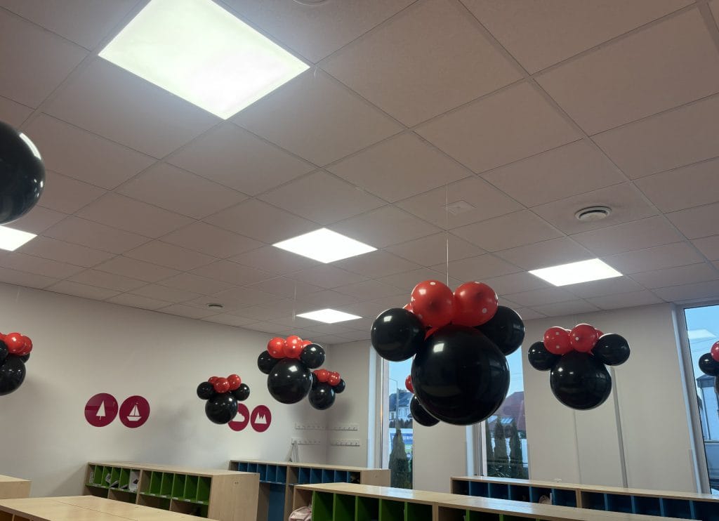 Czarne balony w kształcie głowy Myszki Minnie z czerwonymi kokardami wiszące pod sufitem w sali przedszkolnej