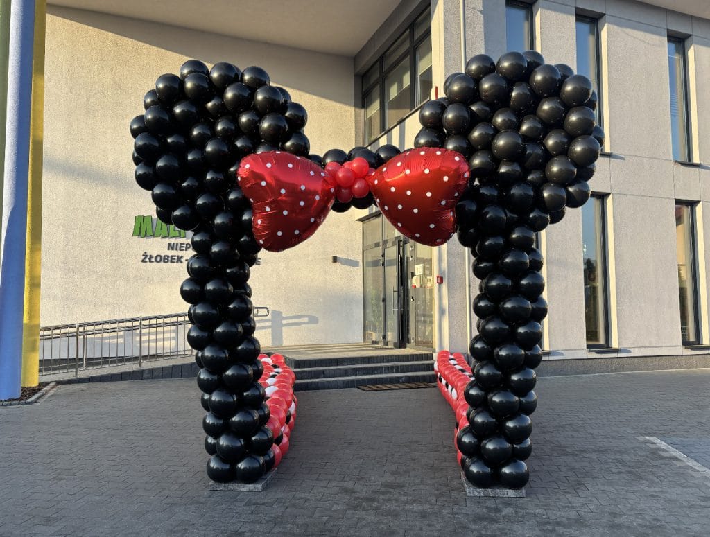 Czarna brama z balonów w kształcie uszu Myszki Minnie z czerwoną kokardą przed budynkiem